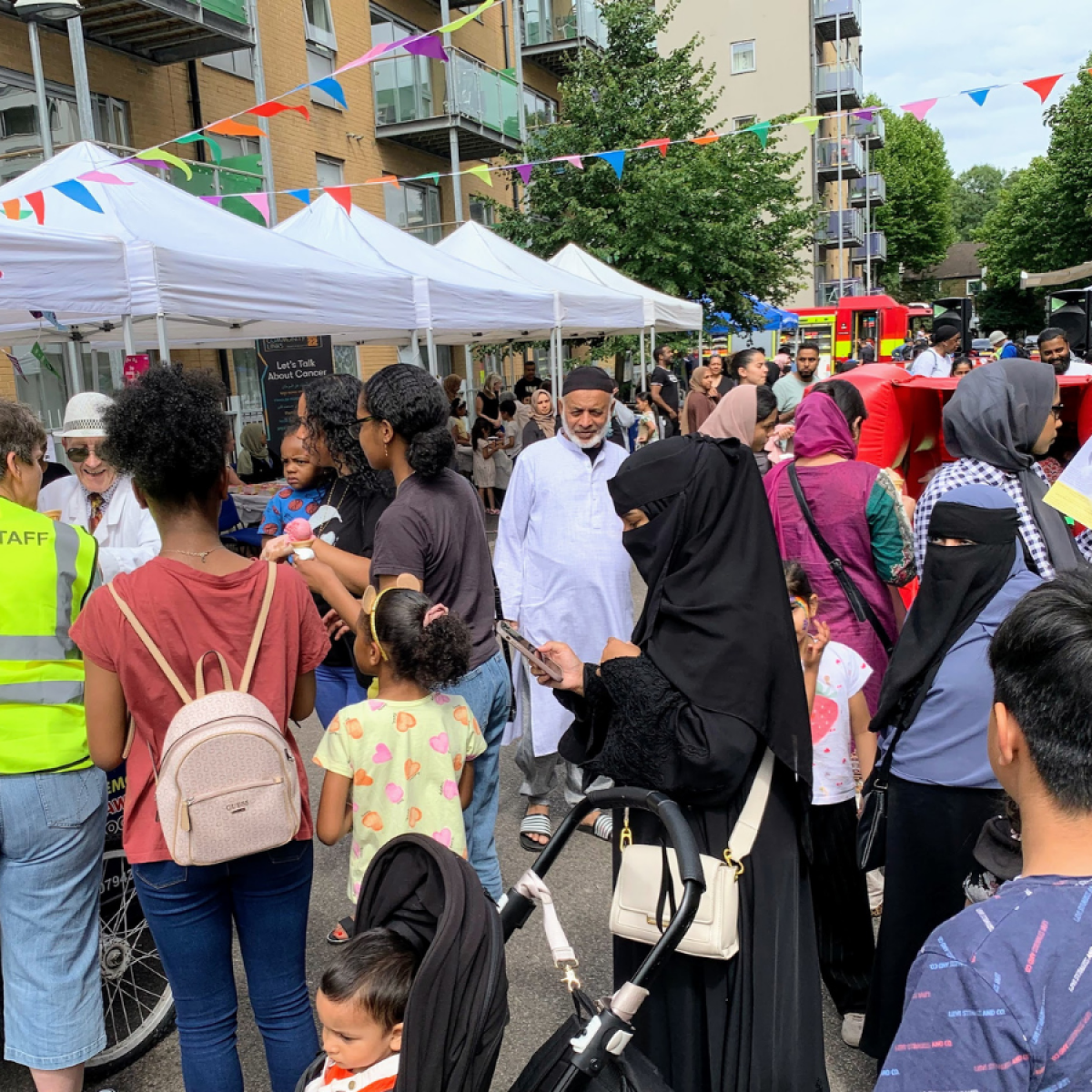 A crowd of local people attend a Summer of Wellbeing street party on a bunting lined street in Bow, E3