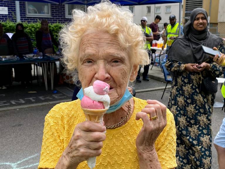 An elderly resident looking summery in a yellow top, enjoying a Well One summer festival and eating an ice cream