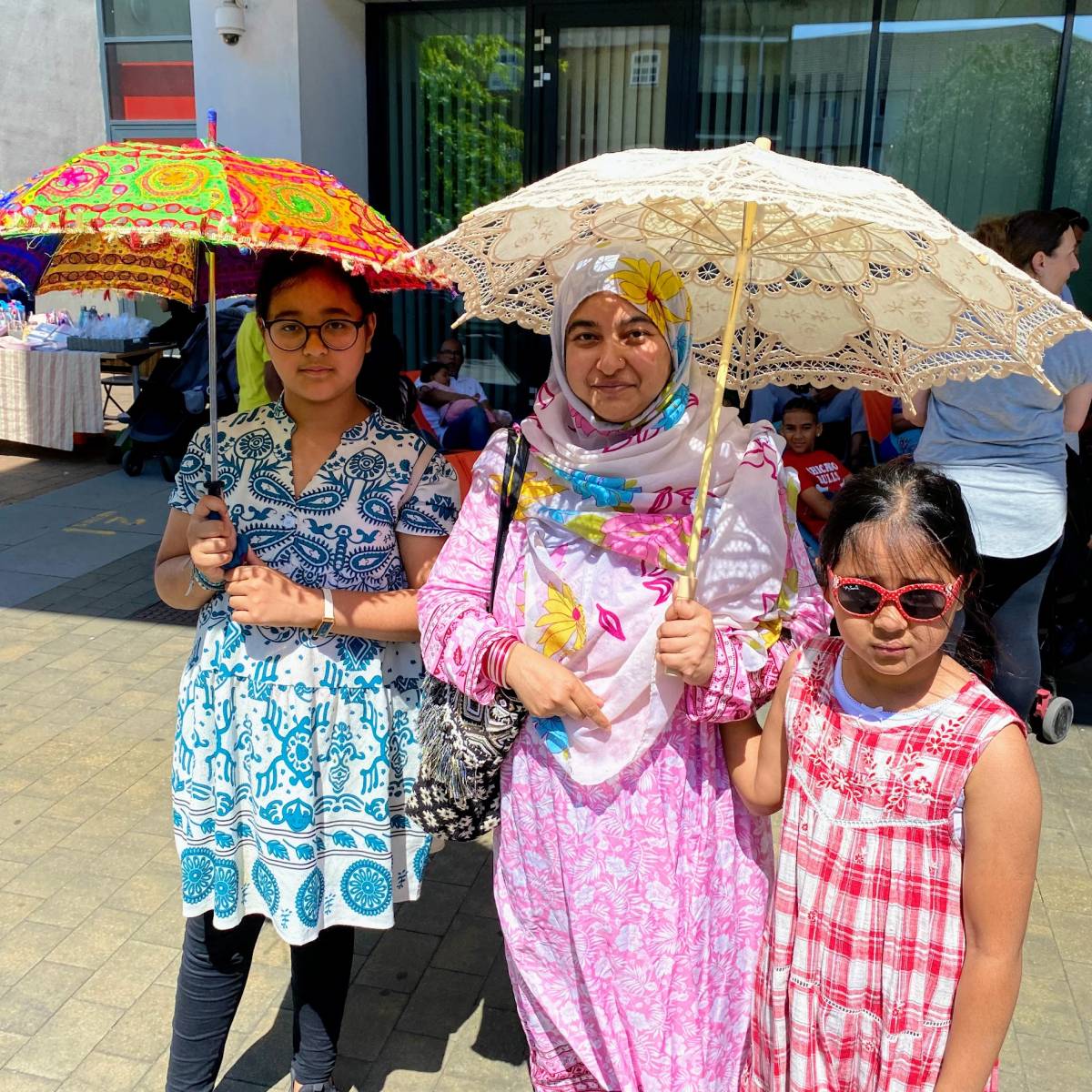A mother and her two young daughters attend the St Paul's Way Summer of Wellbeing Festival, wearing bright patterned clothes and parasols