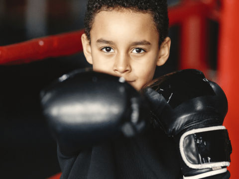 A young boy poses holding up his boxing gloves.
