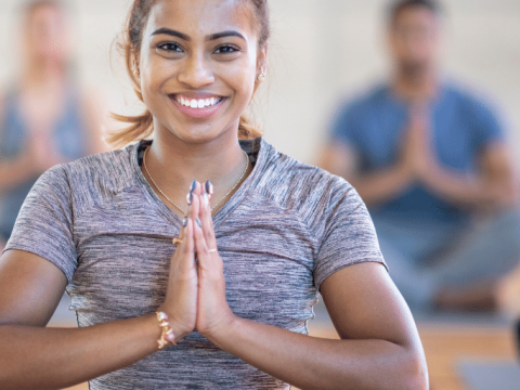 A woman sits cross-legged on a mat in a prayer hands yoga pose.