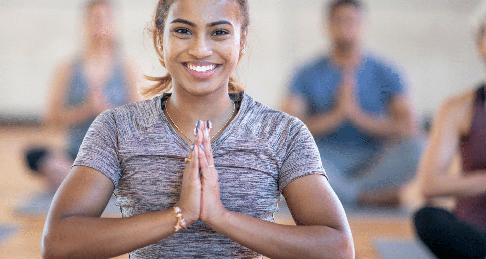 A woman sits cross-legged on a mat in a prayer hands yoga pose.