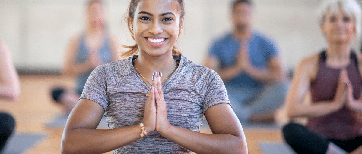A woman sits cross-legged on a mat in a prayer hands yoga pose.
