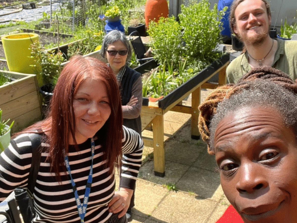 Smiling gardeners taking a group selfie standing by their raised plant beds