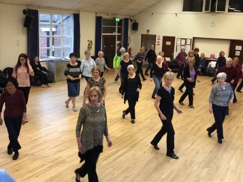 A group of people are line dancing in formation at the Linc Centre