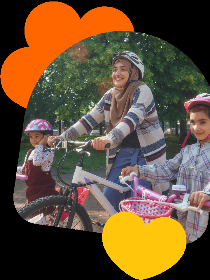Woman cycling with two children in a park, all wearing helmets and smiling