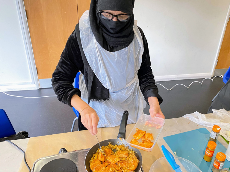 A local woman is frying fish and onions in very little oil at a healthy eating class