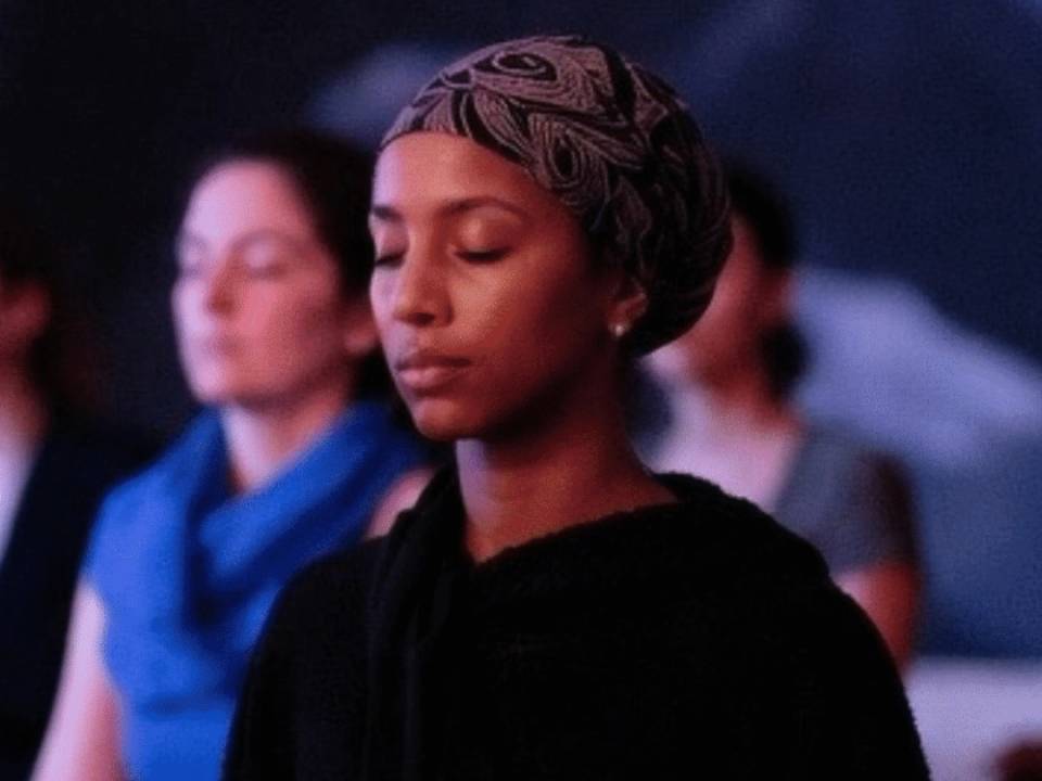 A young woman looks peaceful as she meditates in a wellness class with her eyes closed